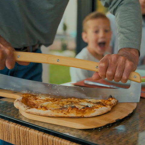 Person using Pi Pizza Rocker Cutter Pro for effortless slicing of thin or thick crust pizza with stainless steel rocker blade.