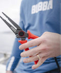 Person holding 8.5 Inch Stainless Steel Pliers With Non Slip Handle, Spring Loaded, Crimp Tool, Side Cutters, Anvil Cutters, Lanyard Hole And Sheath, TiN Coated For Extra Durability And Rust Resistance.