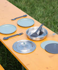 Wildfare Core 12 Piece Stainless Steel Fry Pan Cook Set With 1 Qt Fry Pan Fold and Lock Handle Plates Utensils Spatula BPA Free Camping Kitchen Essentials displayed on picnic table.