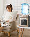 3 In 1 Water Dispenser With Ice Cold Hot And Room Temp Water Mini Desktop Water Cooler For Home Office Dorm Coffee Tea Bar 3 To 5 Gallon Bottle Champagne Gold Finish next to seated woman reading on sofa