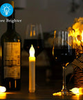 12 Pack Battery Operated Taper Candles With Remote, Warm White Flicker, Flameless LED Handheld on table with wine bottle.