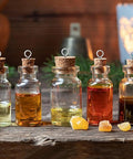Five glass bottles with corks filled with various colored oils on a wooden surface, with amber stones in front and a heart-shaped light in background.