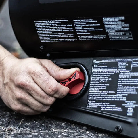 Close-up of hand adjusting variable dial on 60,000 BTU Portable Propane Forced Air Heater With Quiet QBT Technology, black, on textured surface.