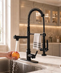 RUMOSE Matte Black Commercial Kitchen Faucets with Pull Down Sprayer in use, rinsing an apple at a kitchen sink.