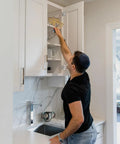 Person reaching into a kitchen cabinet using the Fifty Piece One Half Inch Overlay Soft Close Concealed Cabinet Hinge Set For Face Frame Doors.