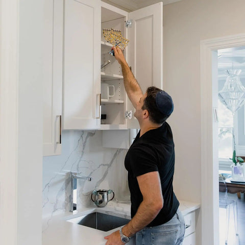 Person reaching into a kitchen cabinet using the Fifty Piece One Half Inch Overlay Soft Close Concealed Cabinet Hinge Set For Face Frame Doors.