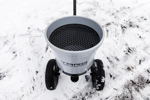 Top view of Beast 50 Lb Walk Behind Spreader For Lawn Care, showing durable composite hopper and clog free grate with wheels on snowy ground.