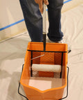 Person using RBC-323 Roll A Bucket With 3 Inch Caster Wheels And Brake 6 Gallon Orange Rolling Bucket For Paint And Tarps