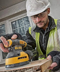 Worker using a 5 Inch 8-Hole Hook And Loop Sanding Pad Replacement Set on an orbital sander indoors, wearing safety gear.
