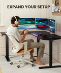 Person using L Shaped Standing Desk 63 By 55 Inches Electric Sit Stand Table With Adjustable Height, gaming setup, black.