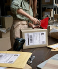 Person organizing parcels with 1500 Count Clear Packing List Envelopes 7x10 Inches Self-Adhesive Shipping Label Sleeves on a table.