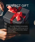 Gift box with red ribbon, beside hands holding a cup and remote, on a dark table.