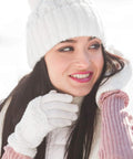 Woman wearing white knitted gloves and hat in snowy weather, smiling outdoors.