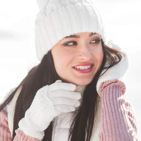 Woman wearing white knitted gloves and hat in snowy weather, smiling outdoors.