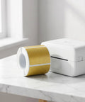 Golden Thermal Label Paper For Shipping And Mailing Self Adhesive Labels With Smooth Surface That Resists Blackening Ideal For Office School And Home Printers Random Color Pack For Easy Labeling next to a white label printer.
