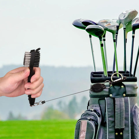 Hand holding retractable club brush with golf bag, part of Two Black Microfiber Waffle Golf Towels With Retractable Club Brush Pro Grade Clean Up For Dirt Mud Sand Grass Must Have Golf Gear And Cleaning Kit For Clubs.