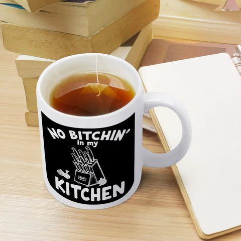 No Bitchin' In My Kitchen 11 Oz Ceramic White Mug on desk with tea, surrounded by books and notebook, Comfortable Handle
