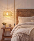 Qingmiao Boho Plug in Pendant Light with handwoven shade hanging above a bed, showcasing a cozy bedroom setting.