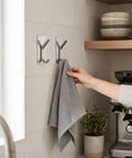 Insane Grip No Drill Towel Hooks Six Pack Silver Rust Proof Heavy Duty Bathroom Wall Mount With Ultra Thick Adhesive Hangs Your Gear Tight And Stays Put For Good holding a gray towel in a modern kitchen.