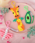 Beads For Crafts Kit With 12 Design Pony Beads And Letter Beads, colorful bead keychains on pink plate, includes giraffe and avocado designs.