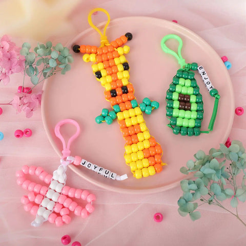 Beads For Crafts Kit With 12 Design Pony Beads And Letter Beads, colorful bead keychains on pink plate, includes giraffe and avocado designs.