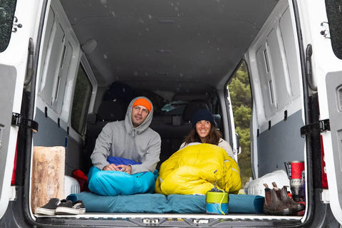 Two people camping in van with gear, including the Two Person Camping Mess Kit With Insulated Mugs in blue and green.