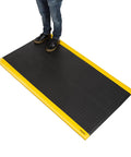Industrial 15/16 Inch Extra Thick Anti Fatigue Floor Mat Built For Heavy Duty Jobs, Diamond Plate Non Slip Ergonomic Standing Mat In Black With Yellow Edge, Perfect For Workbench, Shop, Kitchen, Warehouse 3 By 5 Feet with person standing on it.