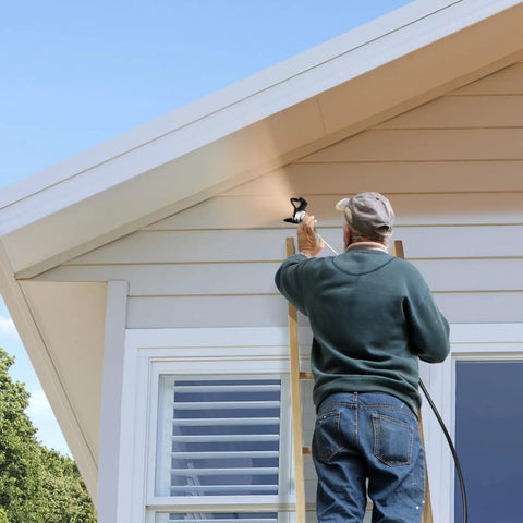 A painter using the Pro Grade High Pressure Electric Airless Paint Sprayer on a house's exterior siding while on a ladder.