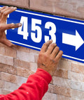 Totally Personalized Metal Street Sign With Your Text Logo Or Photo being installed on brick wall, blue design with arrow and numbers