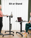 Height Adjustable Rolling Laptop Desk With Cup Holder And Wheels 27 Inch Portable Sit Stand Workstation On Pneumatic Lift Ergonomic Curved Desktop For Comfortable Working Black in use by standing and seated individuals