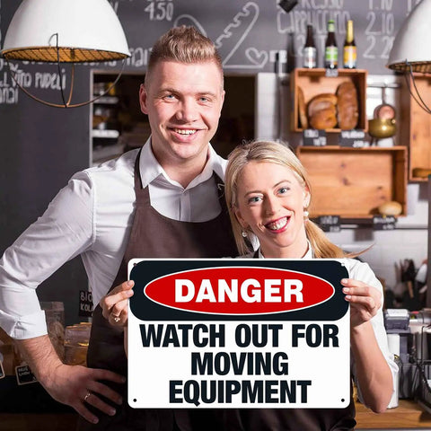 Two people holding a Watch Out For Moving Equipment Sign 8x12 Inch Aluminum Metal Safety Sign in a bakery setting.