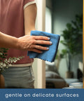 Blue microfiber cleaning cloth held in hand, wiping a bathroom mirror.