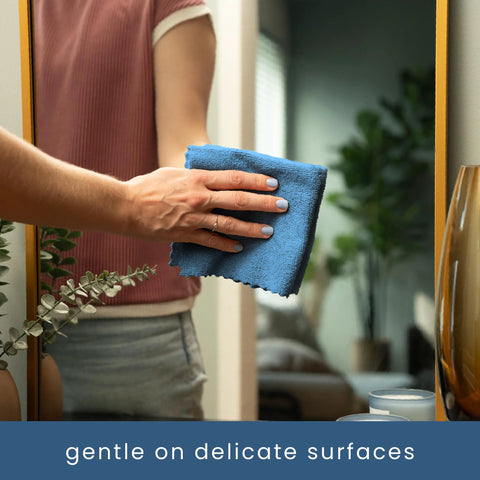 Blue microfiber cleaning cloth held in hand, wiping a bathroom mirror.