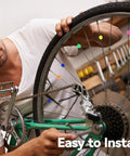 Person attaches Colorful Bike Spoke Beads Kit 144 Pcs Of Glow In The Dark Spoke Lights and Clips to green bicycle wheel