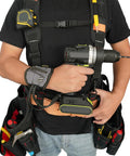 Person wearing a tool belt suspenders with magnetic wristband for framer carpenter electrician worksite ready all day comfort 4 point support padded backing breathable straps adjustable fit gray holding a drill