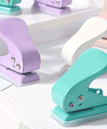Compact colorful single hole punchers for card making, scrapbooking, and crafts shown in purple, white, and teal on a light surface.