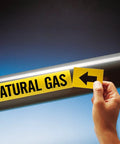 Self Adhesive Pipe Markers For Natural Gas 1X8 Inch Black And Yellow Labels on pipe, hand applying label with arrow.
