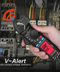 Hand using Pro Grade 1mA Resolution DC Clamp Meter True RMS Digital Multimeter highlighting V-Alert feature in electrical panel.