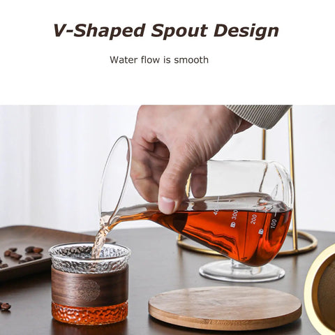 Person pouring from a glass vessel with V-shaped spout into a decorative cup, showcasing the Kickback Cold Brew Dripper Coffee Tower.