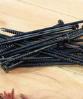Pile of black timber screws on wood surface, resembling Exterior Timber Screws Workhorse 0.220 Inch By 5 Inch Double Barrier Coated