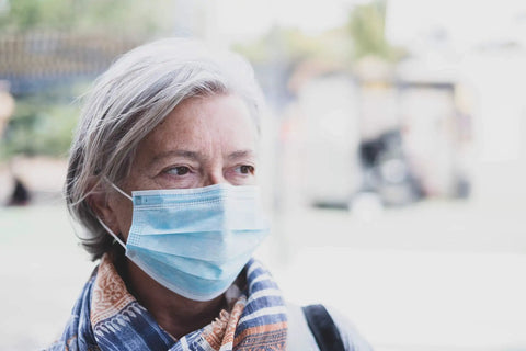 Person wearing a blue Disposable 3 Ply Face Masks Pack Of 50 Breathable Ear Loop Masks In Blue For All Day Comfort With Adjustable Nose Piece Perfect For Work, School, Travel, And Everyday On The Go Protection. Outdoors, neutral background.
