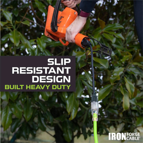 Weatherproof 100 Ft Outdoor Extension Cord with Lighted End in use with orange power tool near greenery