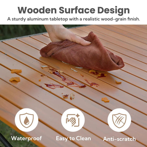 46.4 Inch Large Camping Table For Two To Six People Beefy Built Heavy Duty Foldable Aluminum Roll Up Top Carry Bag 220lbs Capacity Portable For BBQ Tailgating Backyard Natural Finish with a wooden surface design being cleaned with a cloth showing its waterproof and easy-to-clean features.