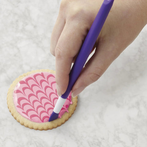 Hand using Top Shelf Cookie Decorating Tools Set Featuring Etching Wand on pink decorated cookie.