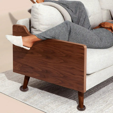 Close-up of a light brown felt chair leg pad and caster cup installed on couch leg on hardwood floor.