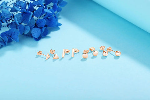 Rose Gold Unisex Stud Earrings Set For Women And Men 4 Pairs Of Dope Comfortable Studs In Circle Triangle Ball Shapes With 7.5mm Bars And 10mm Posts Easy Secure Butterfly Backs Hypoallergenic And Safe Everyday Wear. four rose gold stud earring pairs on blue background