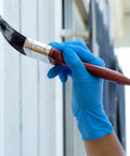 Blue nitrile disposable glove on hand painting a white wall with a brush