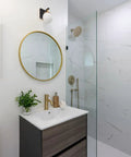 Bathroom interior with Alluria Wall Sconce Weathered Black With Autumn Gold Finish, round mirror, and glass shower