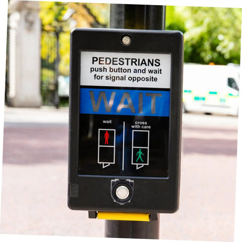 Pedestrian crossing signal with wait button, covered by round button protector, on a street post, outdoors.