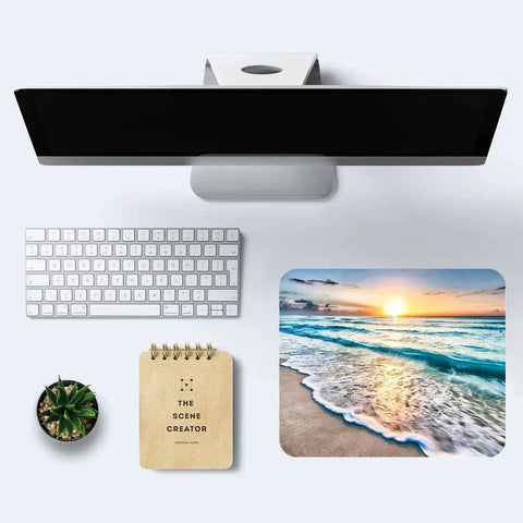 Overhead view of a Coastal Sunset Themed Mouse Pad For Laptop And Desktop Cute Customizable Small Desk Pad With Non Slip Rubber Base Ultra Smooth Surface Portable Office Accessory For Work From Home And Travel Dope Gift Idea next to a white keyboard, notebook, and small plant on a desktop.